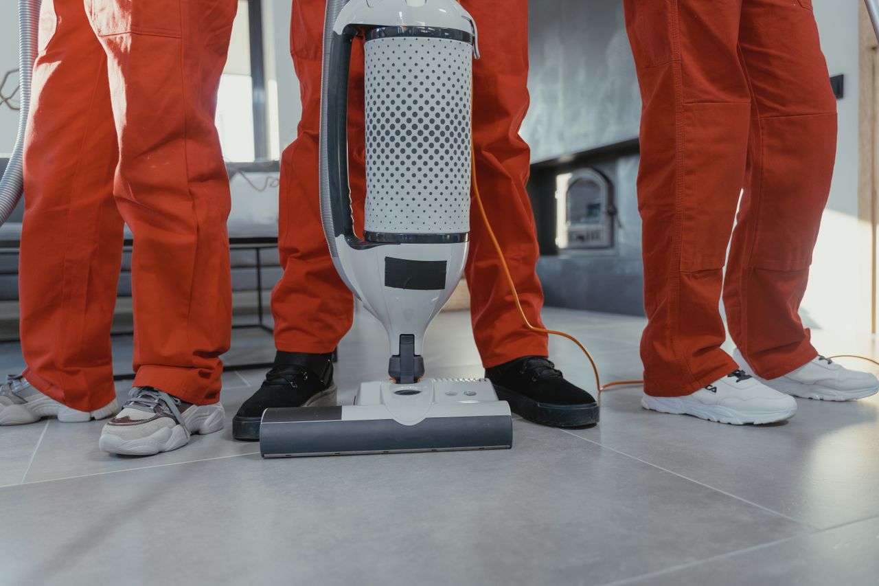 Équipe de nettoyeurs professionnels en uniformes rouges utilisant un aspirateur à l’intérieur.